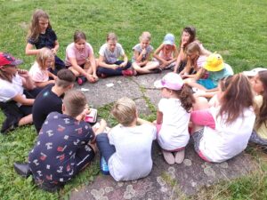 Skupina dětí sedí v rodinném kruhu a povídá si na letním dětském táboře. 