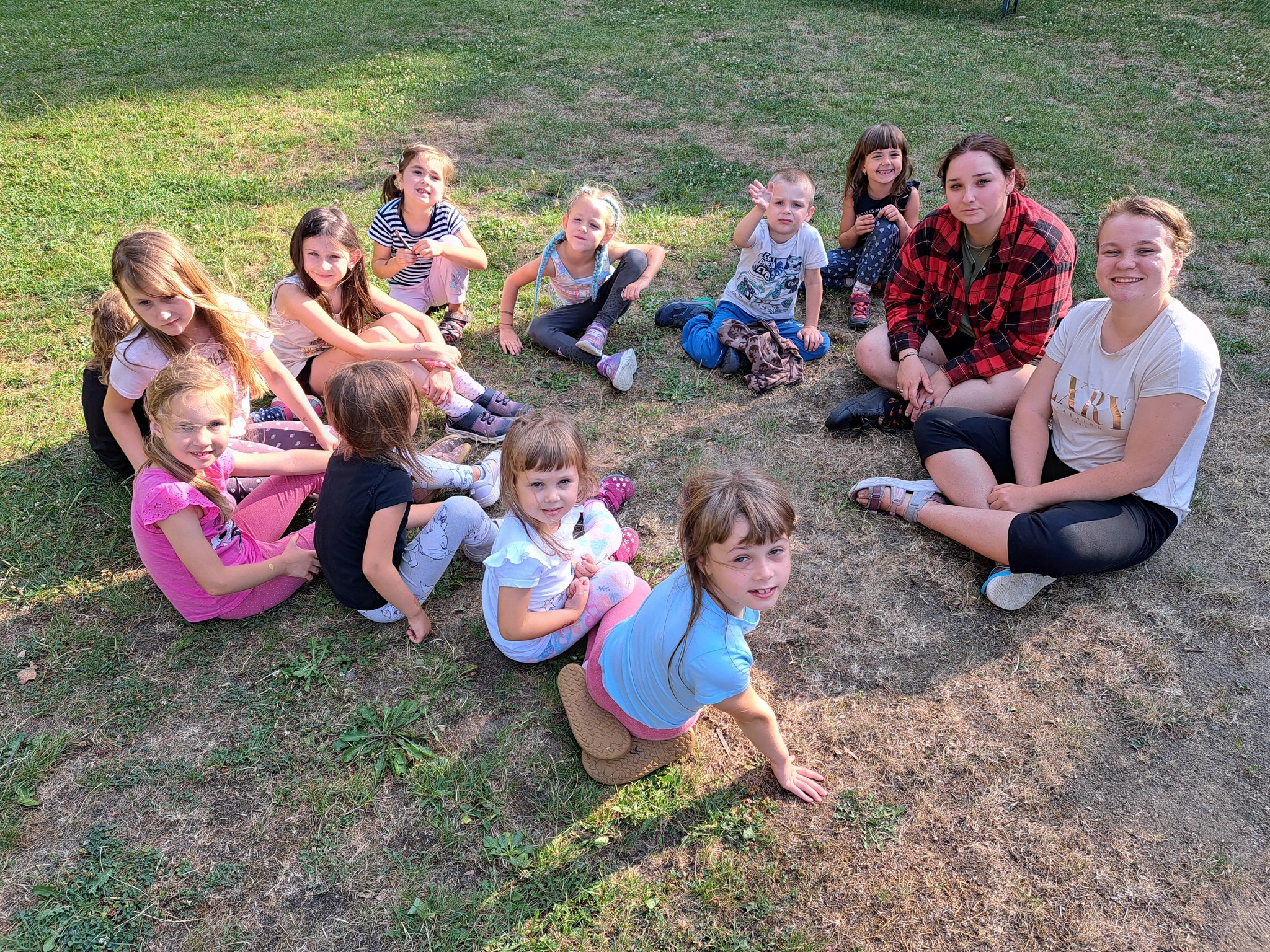 Děti sedí v přírodě na letním táboře pro nejmenší děti.