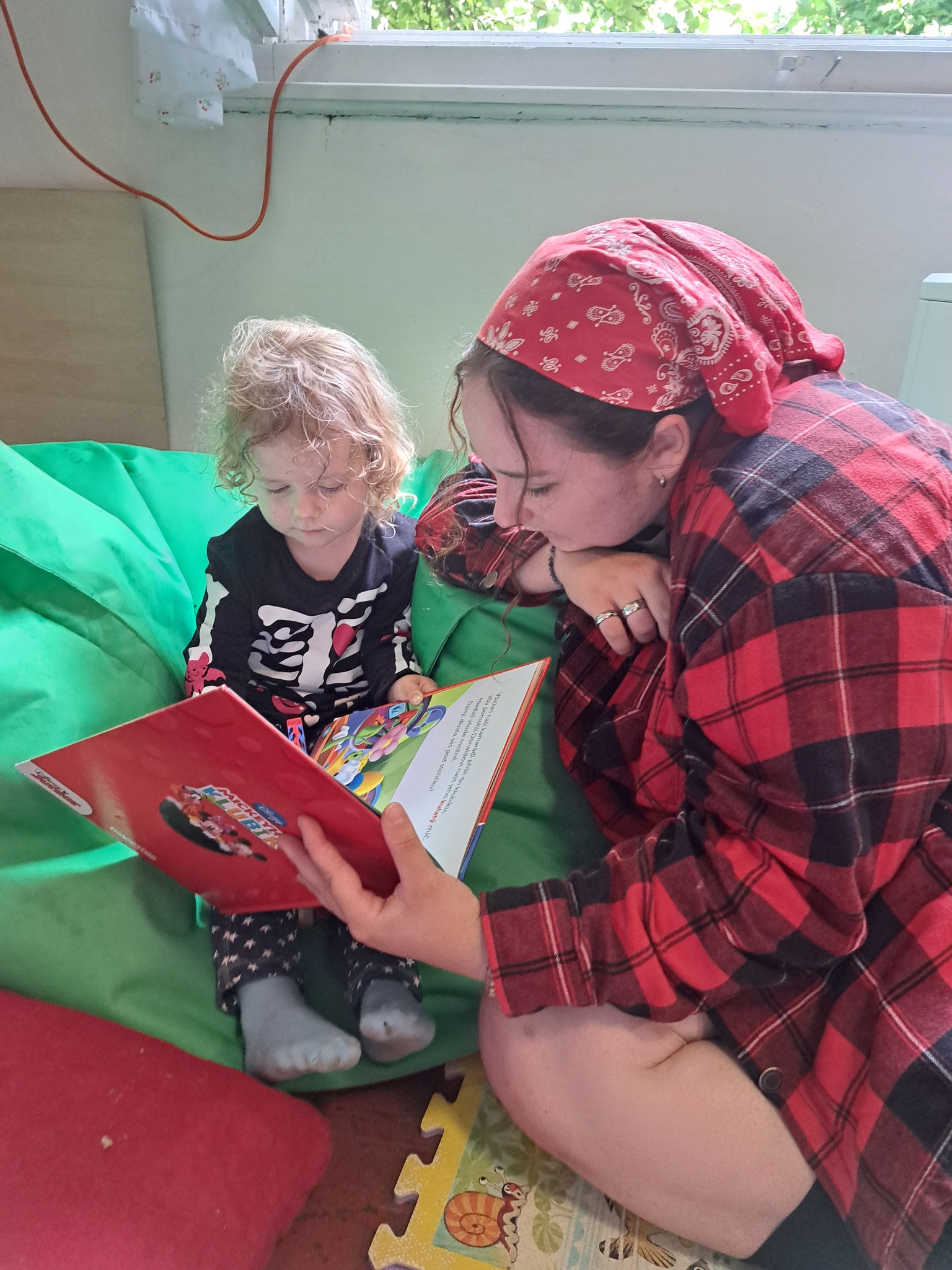 Vedoucí čte dětem na letním táboře pro nejmenší pohádkovou knížku v herně.