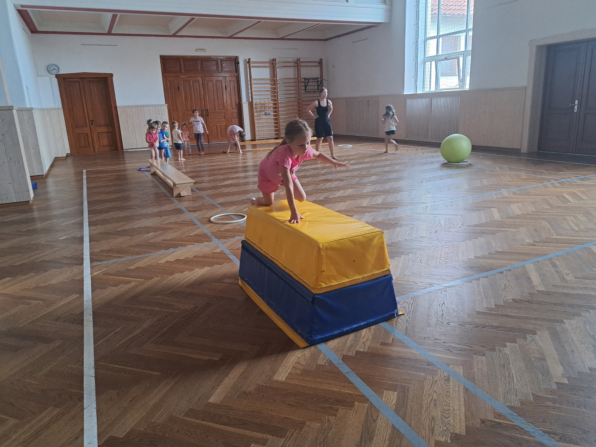 Děti sportují na letním táboře pro nejmenší v tělocvičně s kvalitními pomůckami.