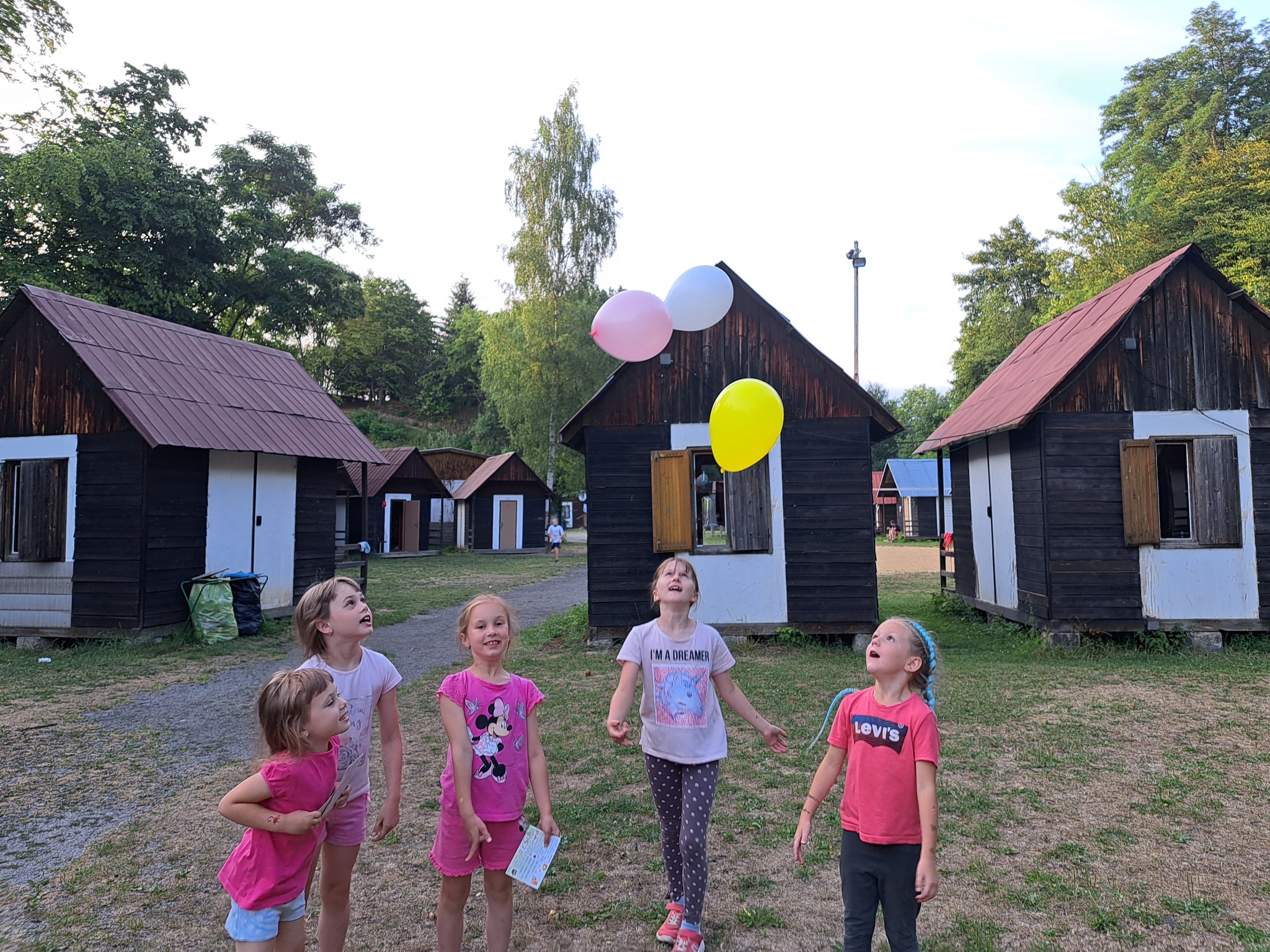 Dívky na letním dětském táboře si hrají s nafukovacím míčkem v táborové základně.