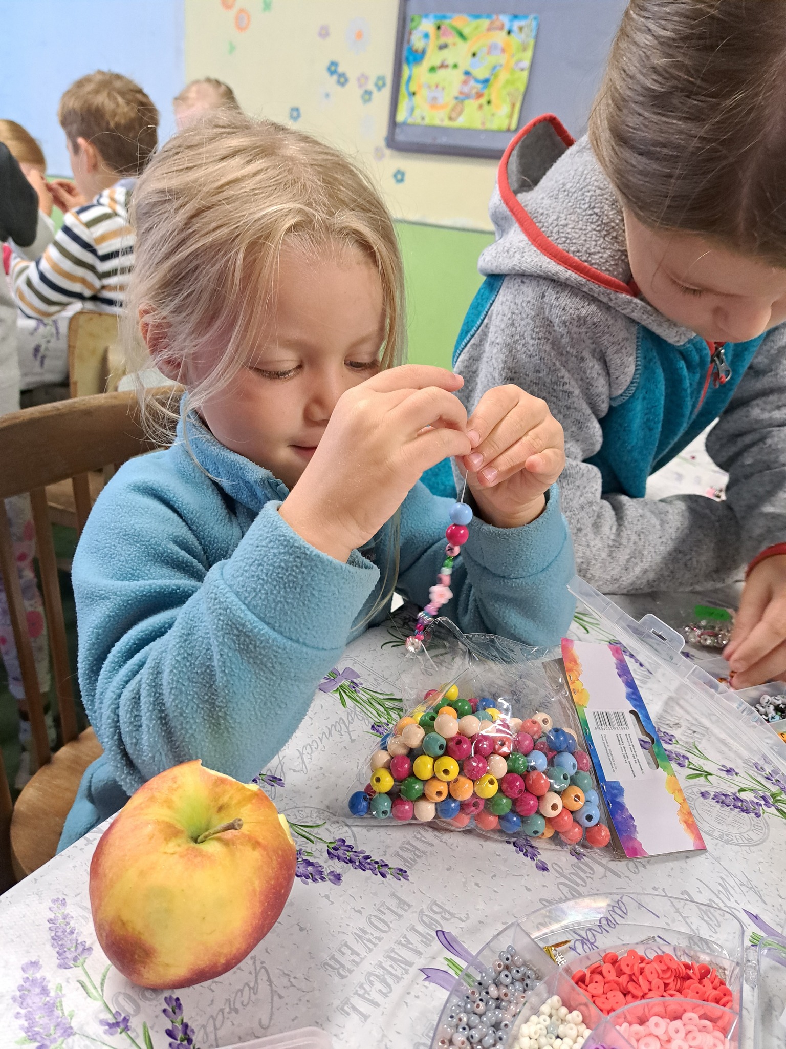 Děti na letním výtvarném táboře navlékají korálky a kreslí v jídelně.