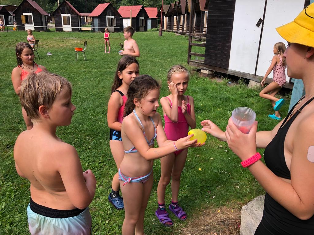 Děti po sobě hází balónky s vodou na letním dětském táboře.