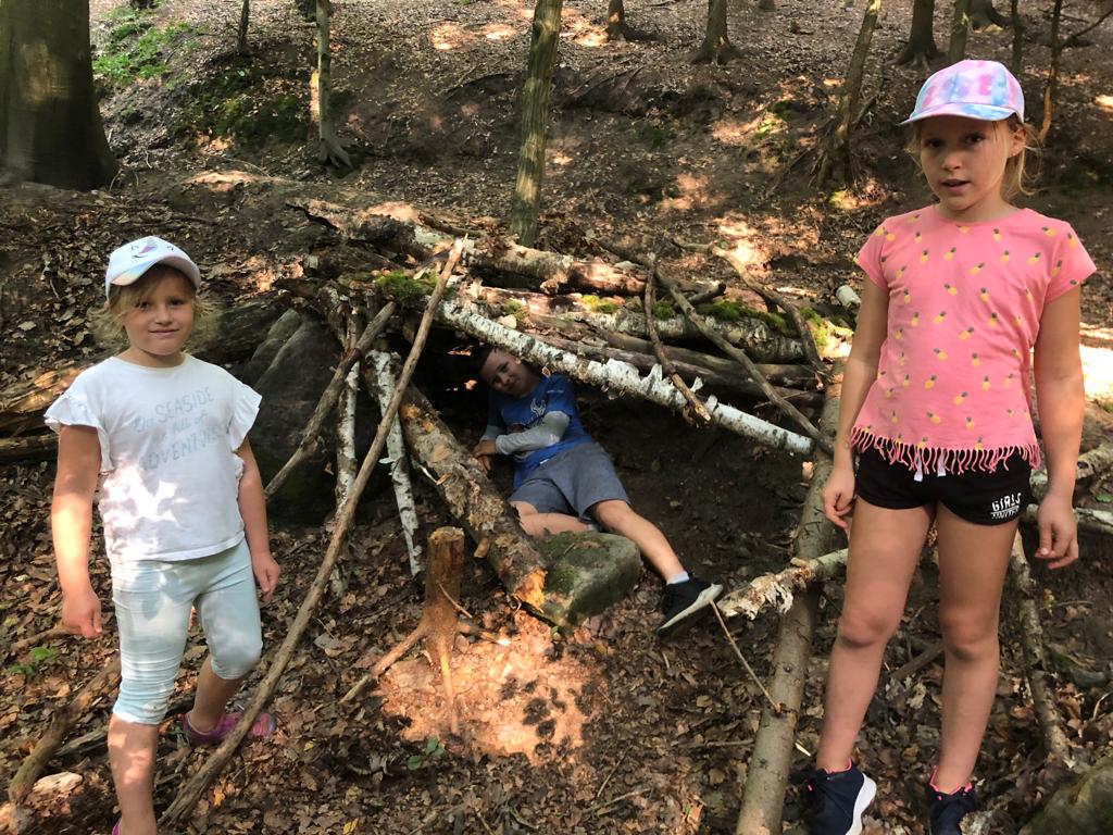 Děti staví v lese domečky z větví, listí a jehličí na dětském letním táboře.