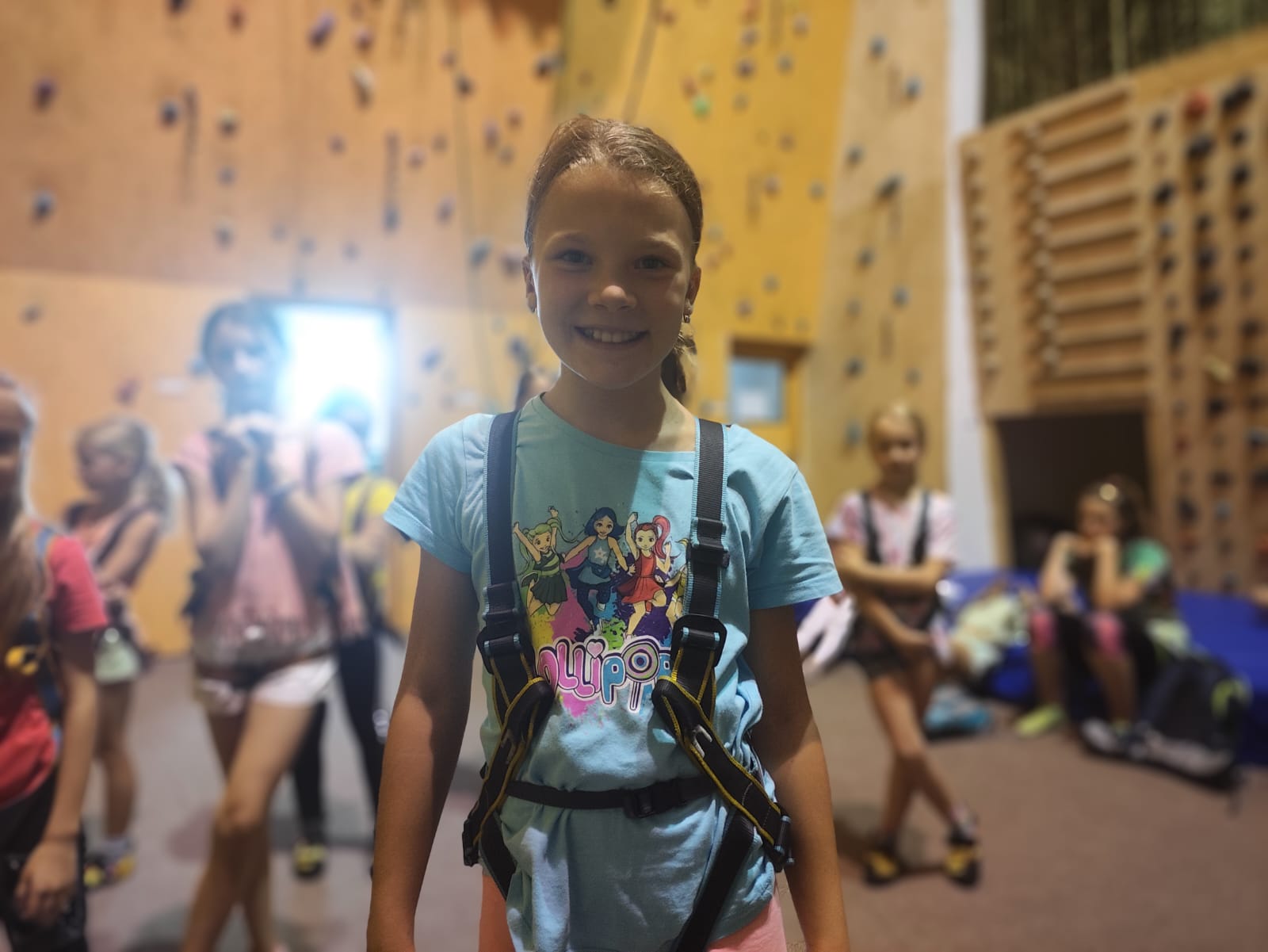 Dívka zkouší lézt na lezecké stěně na letním dětském táboře.