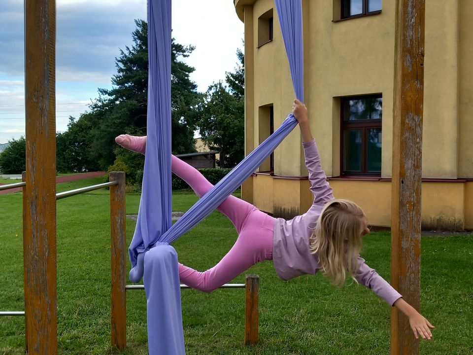 Děti na letním cirkusovém táboře cvičí na gymnastické šále vzduchovou akrobacii.