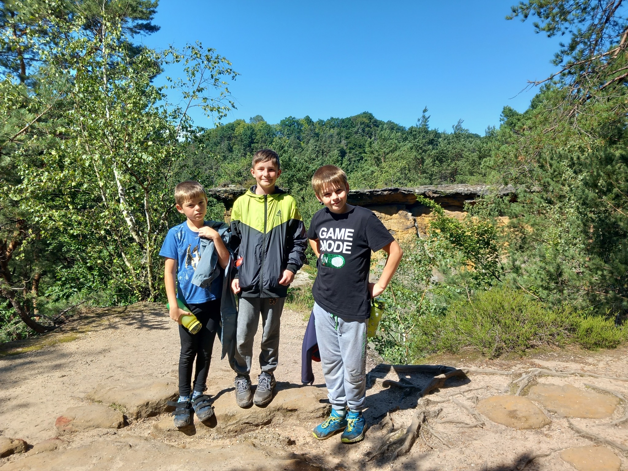 Děti na letním dětském táboře chodí v přírodě a hledají kešky poblíž skalního útvaru Pokličky.