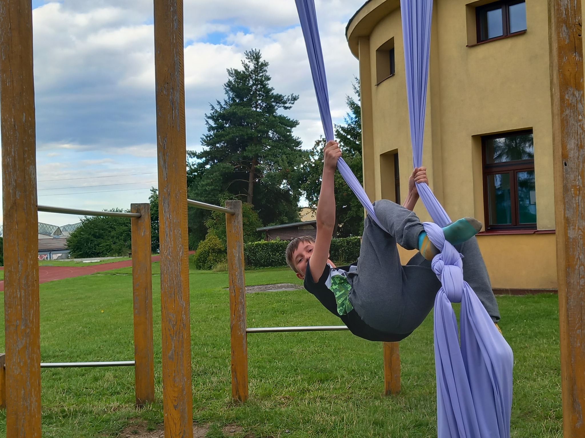 Děti na letním cirkusovém táboře cvičí jako artisté vzduchovou akrobacii.