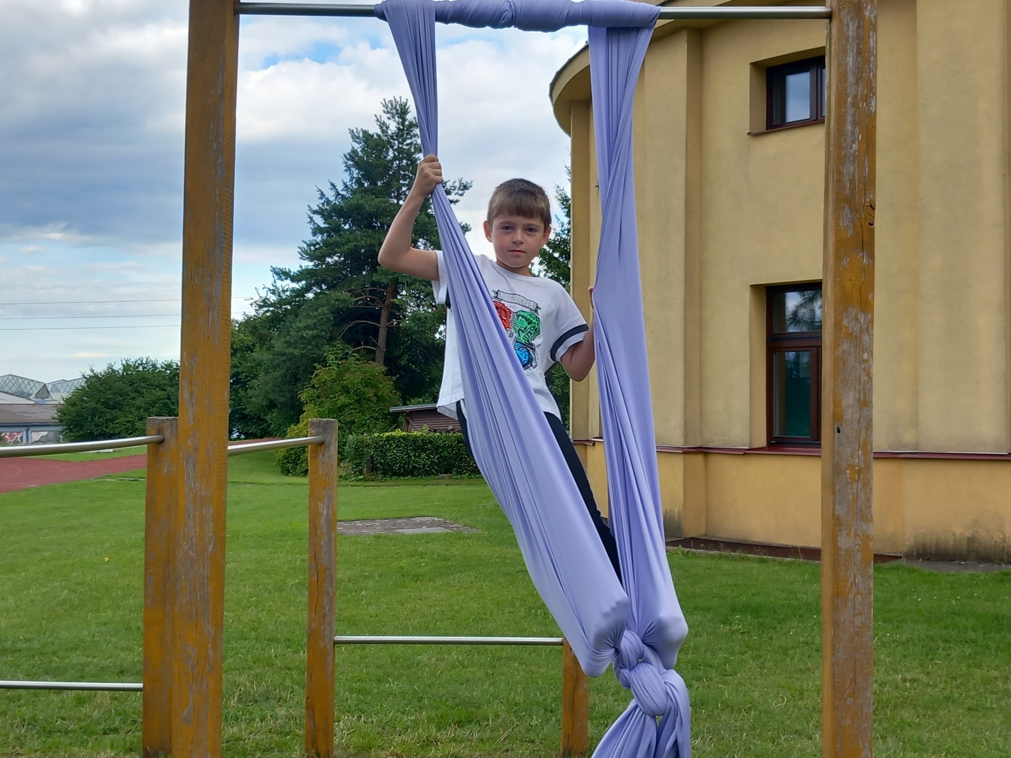 Děti na letním cirkusovém táboře cvičí jako artisté vzduchovou akrobacii blízko školy.