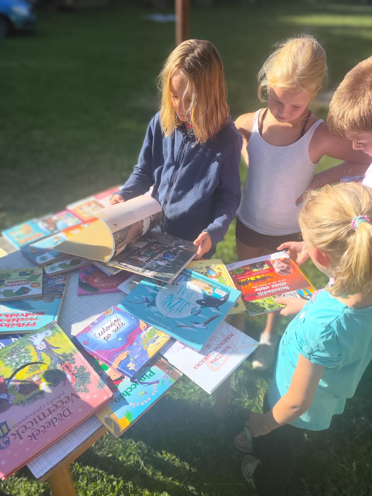Děti na letním uměleckém táboře si čtou knížky v přírodě.