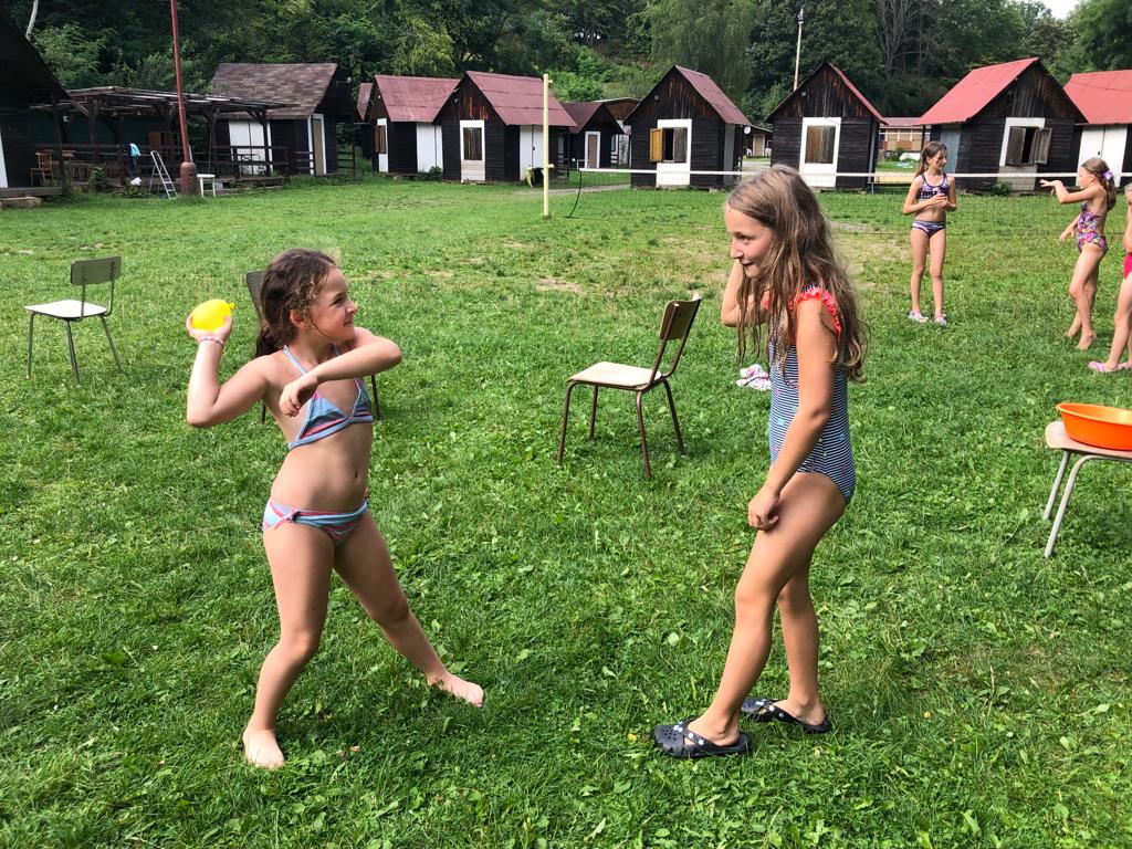 Děti na letním hudebním táboře si hrají s vodou v plavkách a koupají se.