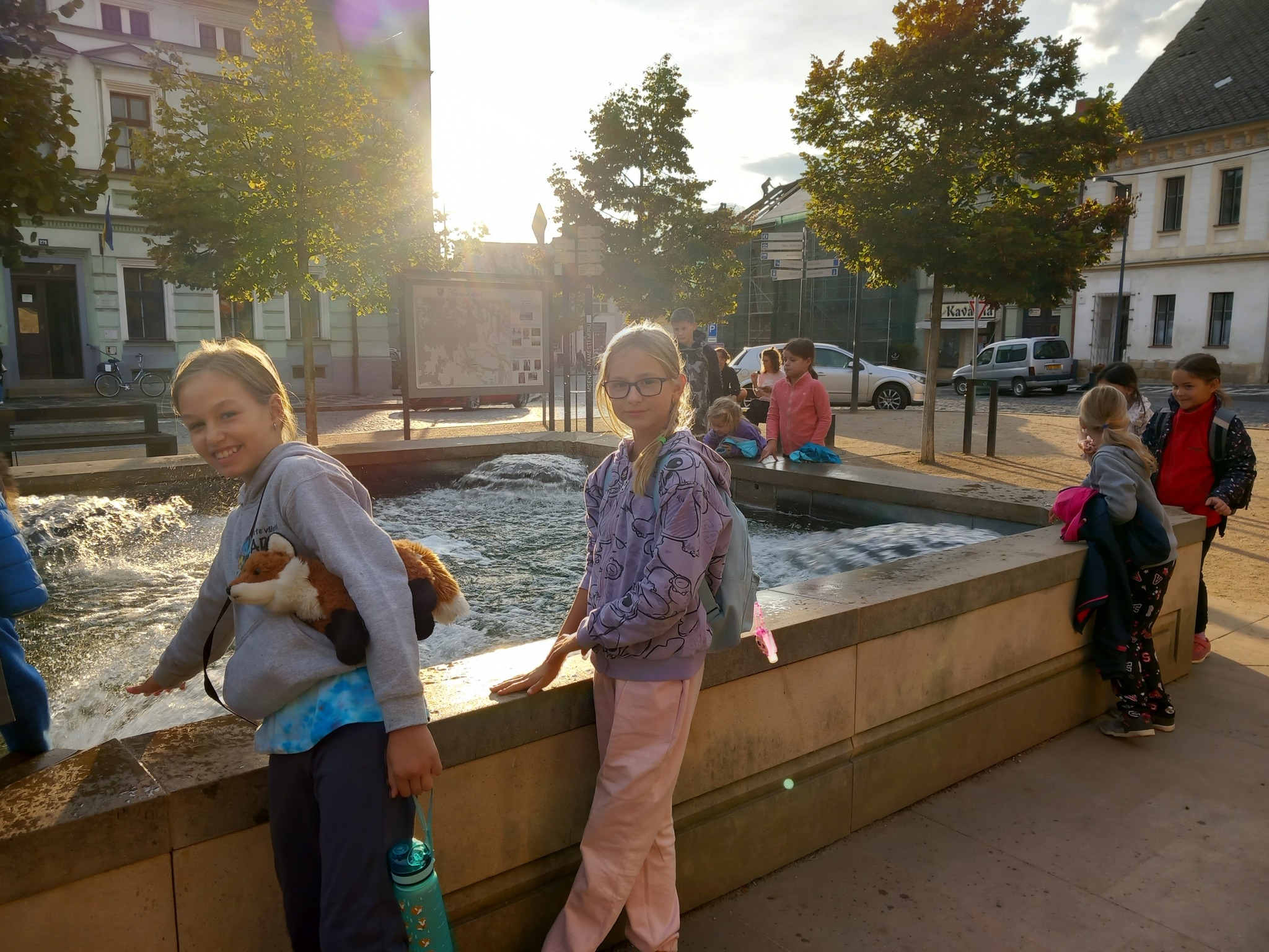 Děti na letním dětském táboře jsou na návštěvě ve městě a hrají si s vodou v kašně.