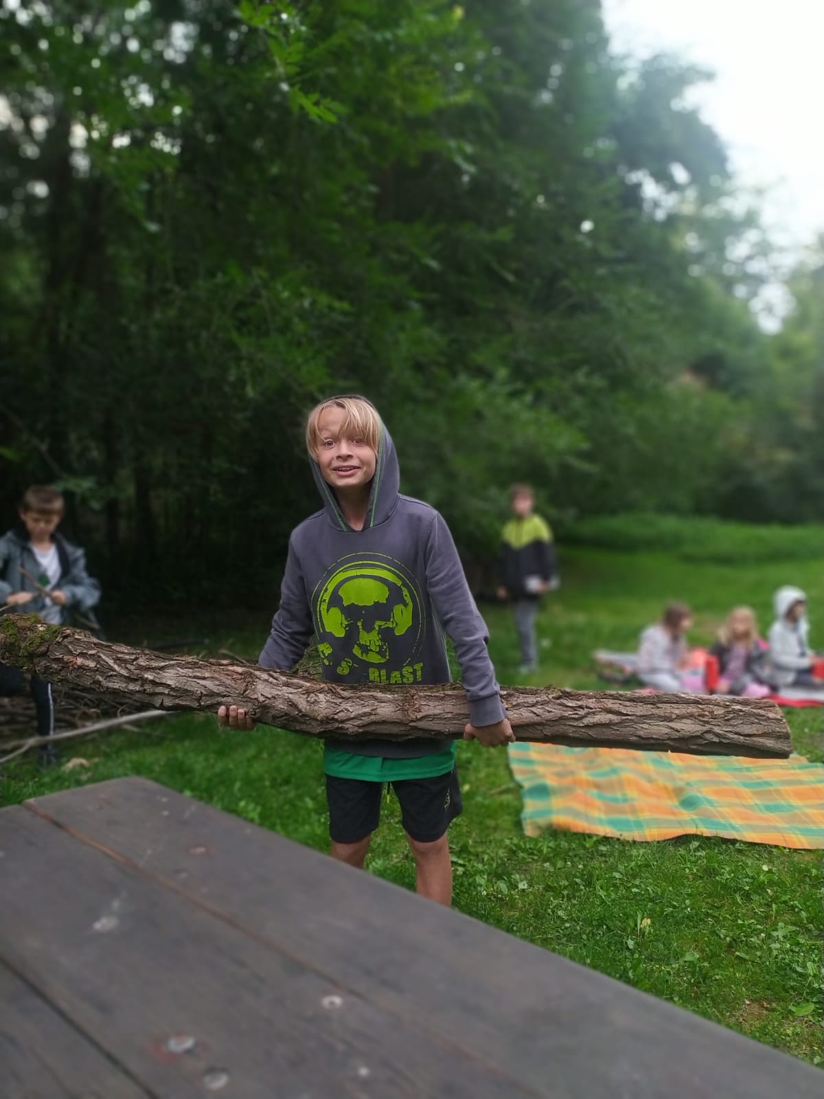 Chlapec na kutilském táboře nese velkou kládu jako dřevo na táborák.