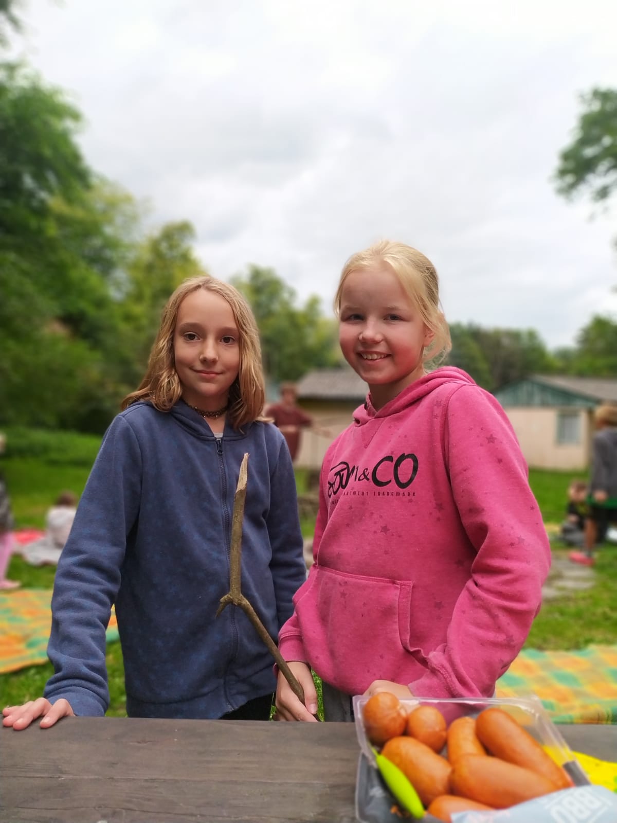 Dívky na letním příměstském táboře si opékají buřty u táboráku.