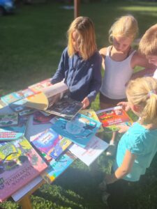 Děti si čtou knihy v přírodě na letním dětském táboře.