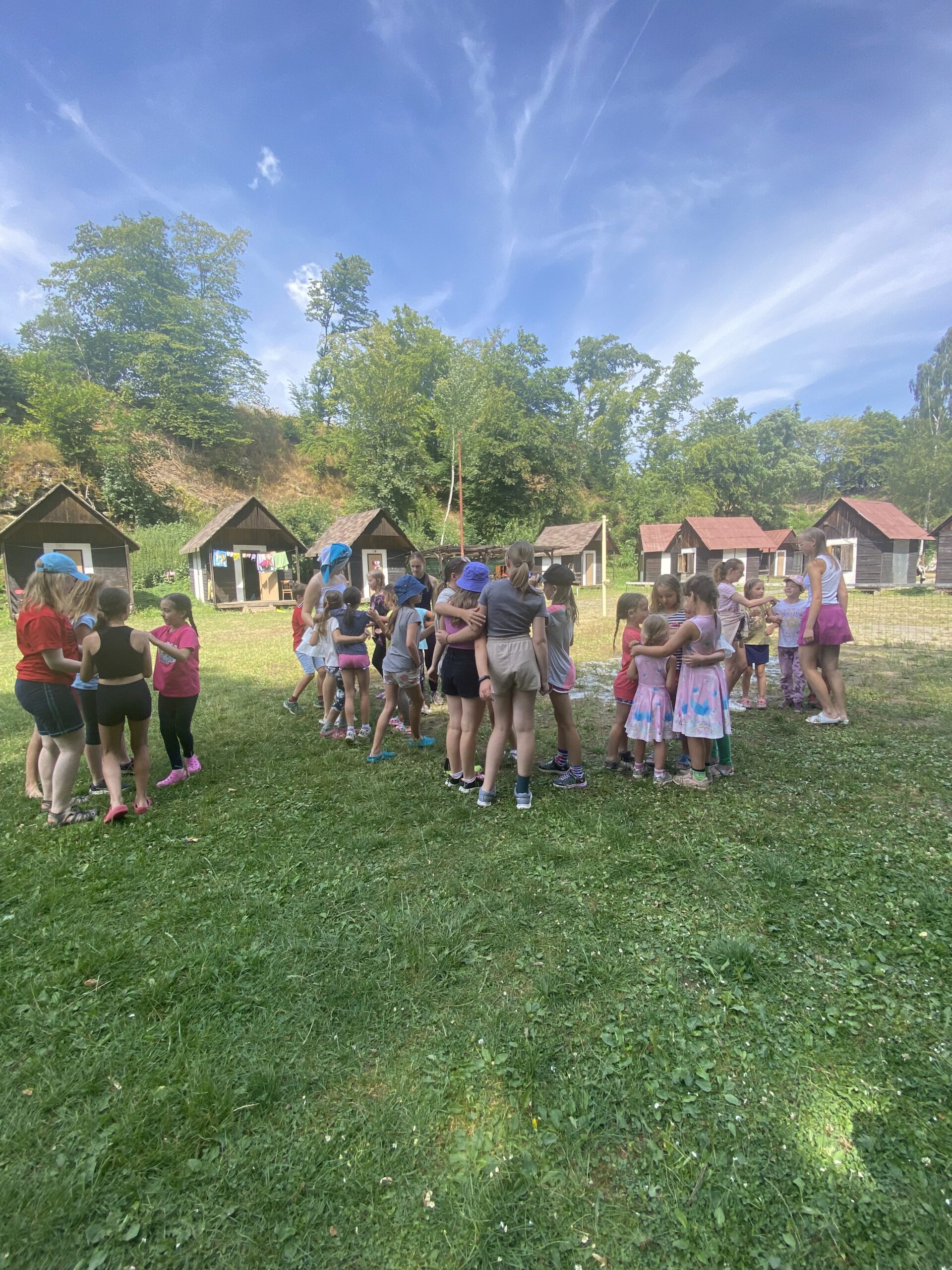 Děti stojí ve skupinkách v přírodě na letním dětském táboře.