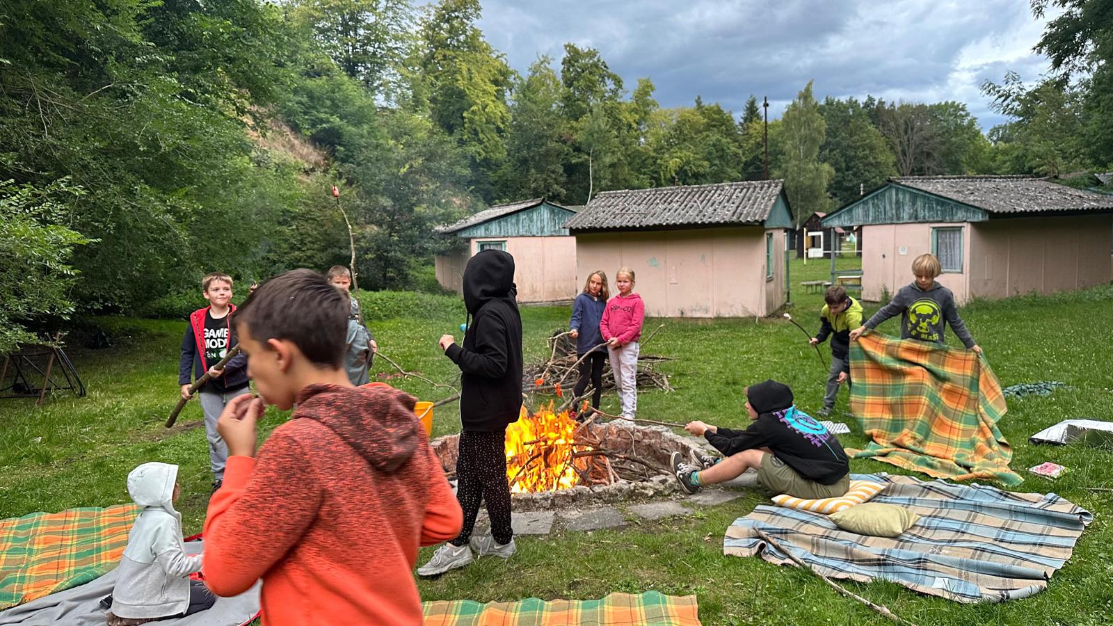 Děti opékají špekáčky na táboře.